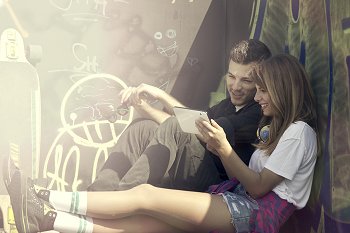 Studentin und Student sitzen auf einer Mauer in der Sonne und schauen auf ein Tablet