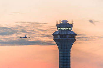 Ein Flugzeug fliegt an einem Tower vorbei, während der Himmel eine zartorgangene Farbe hat
