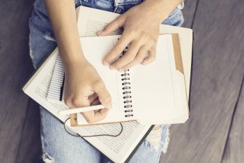 Vertriebsingenieurwesen Studieninhalte Studentin sitzt auf Boden, auf ihren Beinen Bücher und Notizbuch